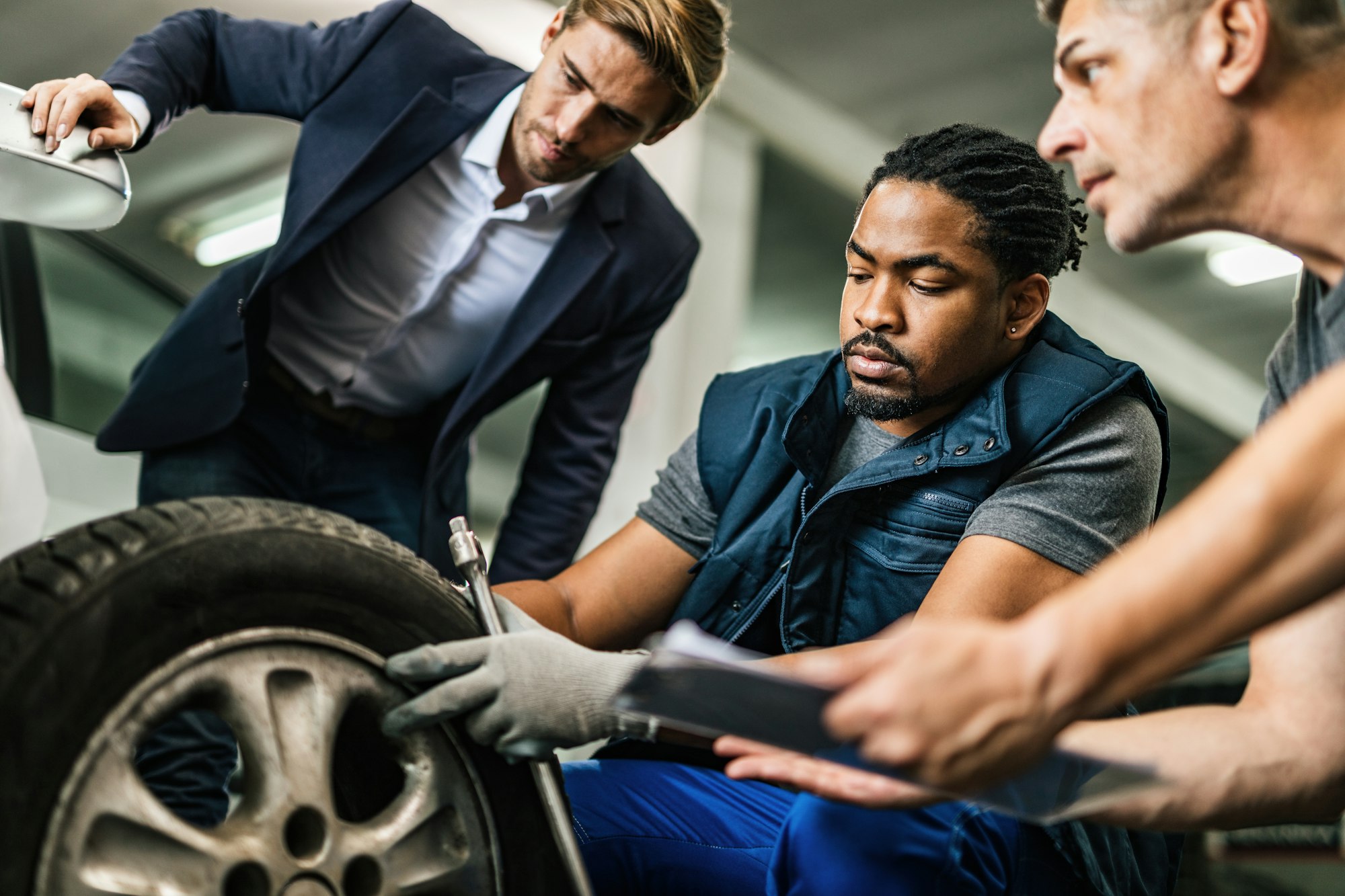 Auto mechanics repairing tire of customer's car at repair workshop.